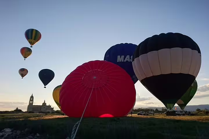 Colorful hot air balloons preparing for liftoff in Segovia, set against a picturesque sunrise and historic architecture.