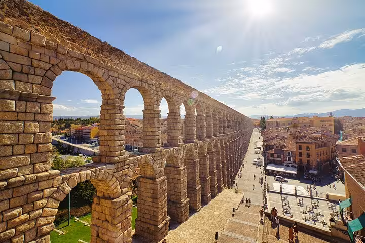 View of Segovia's ancient Roman aqueduct under a bright sun, highlighting its impressive arches and historic charm.