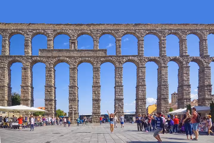 Visitors admire the ancient Roman aqueduct in Segovia on a sunny day, highlighting this iconic stop on the El Escorial tour.