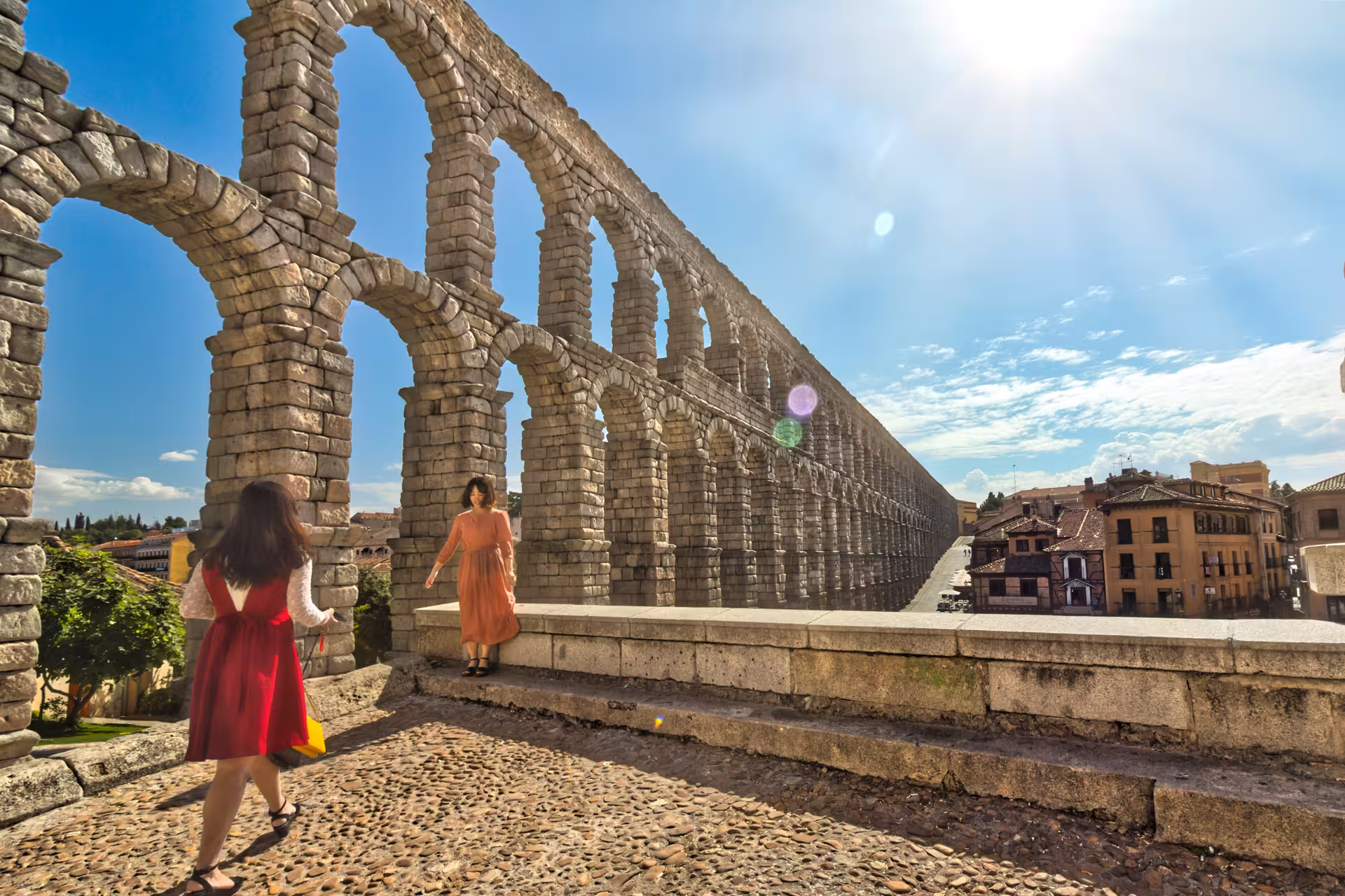 Tourists explore the historic Roman Aqueduct of Segovia under a bright blue sky on a full-day trip from Madrid.