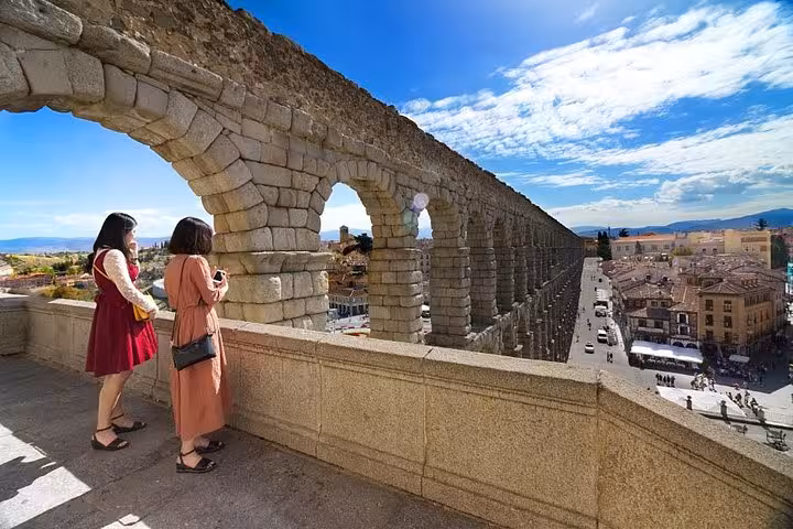 Tourists admire the historic Roman aqueduct in Segovia under a bright blue sky on a half-day trip from Madrid.