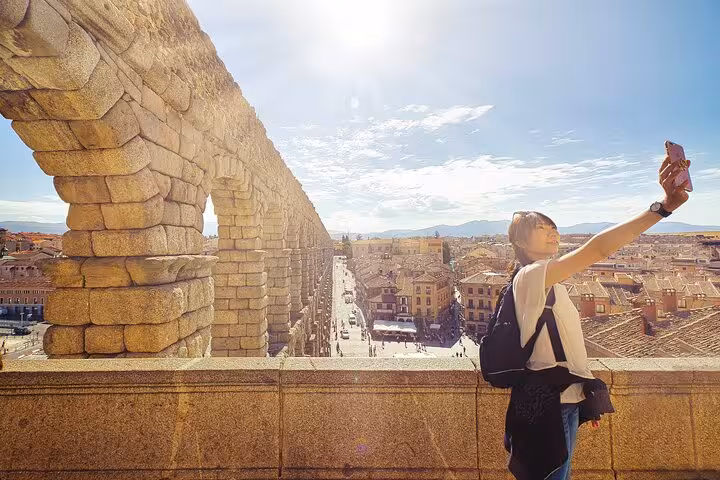 Visitor capturing a selfie at the iconic Roman aqueduct in Segovia under the bright sun.