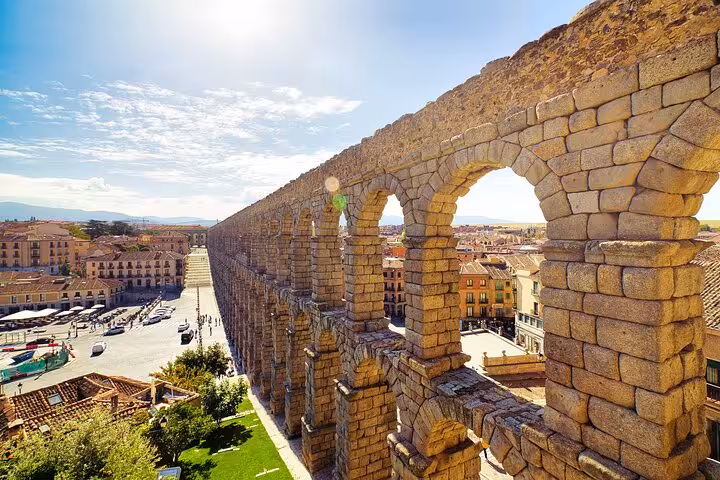 Sunlit Roman aqueduct in Segovia, showcasing its impressive arches and the surrounding city view.
