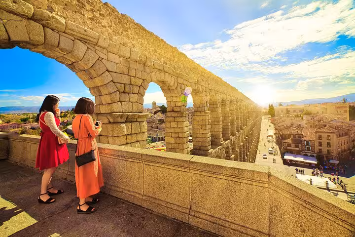 Tourists admire the historic Roman Aqueduct of Segovia at sunset on a day trip from Madrid with gourmet lunch option.
