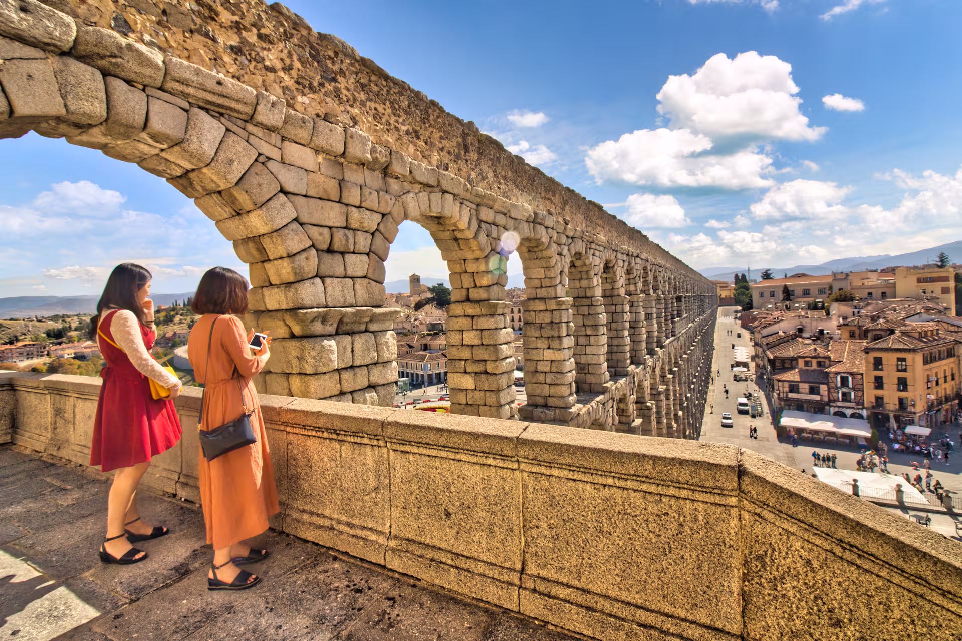 Visitors admire the expansive view of the Roman aqueduct and Segovia's charming townscape under a bright sky.
