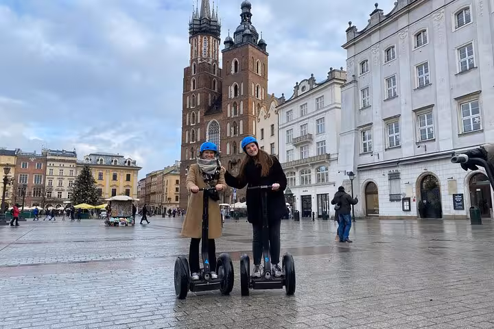 Two people on Segways explore Krakow's Main Market Square with St. Mary's Basilica in the background, perfect for city tours.