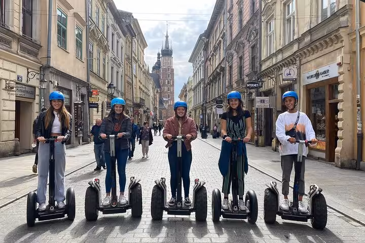 Five friends on Segways touring Krakow's Old Town, surrounded by charming cobblestone streets and architecture.