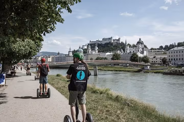 Segway tour group cruising along the Salzach River with a backdrop of Salzburg's iconic castle and cityscape.