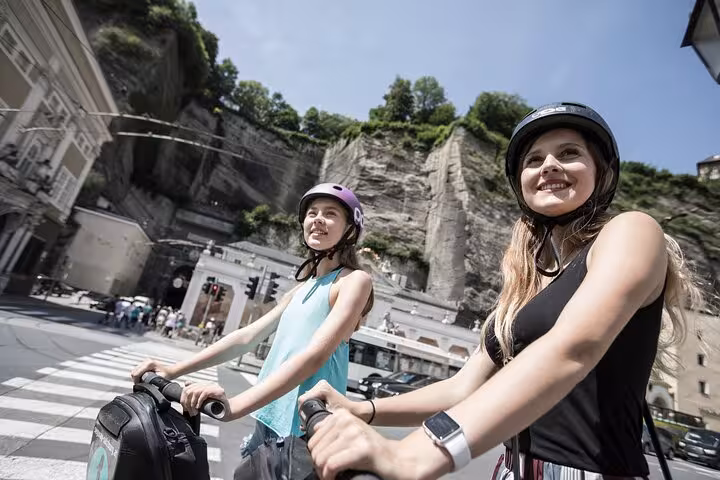 Two women on a Segway tour in Salzburg, smiling as they explore the city’s picturesque streets and rocky backdrop.