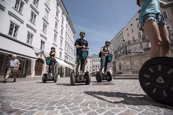 Segway riders touring a picturesque cobblestone square in Salzburg under a clear blue sky.