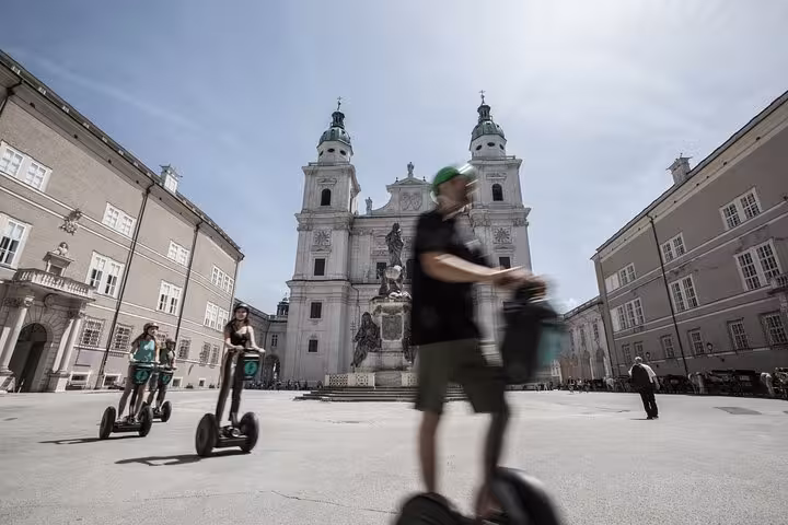Tourists on Segways explore Salzburg's historic square, with stunning cathedral views on a sunny city tour.