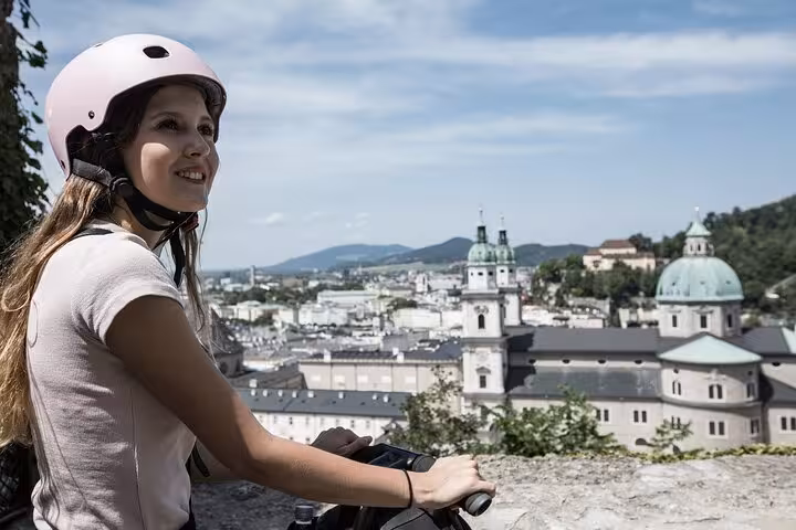A woman on a Segway admires the panoramic view of Salzburg's skyline and historic architecture on a sunny day.