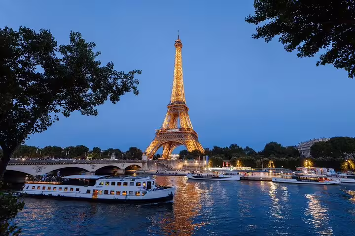 Illuminated Eiffel Tower at dusk with Seine River dinner cruise boats passing below