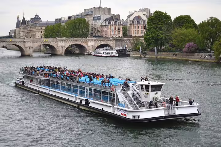 Packed tourist river cruise boat sailing on the Seine River with Paris historic buildings and bridge in background