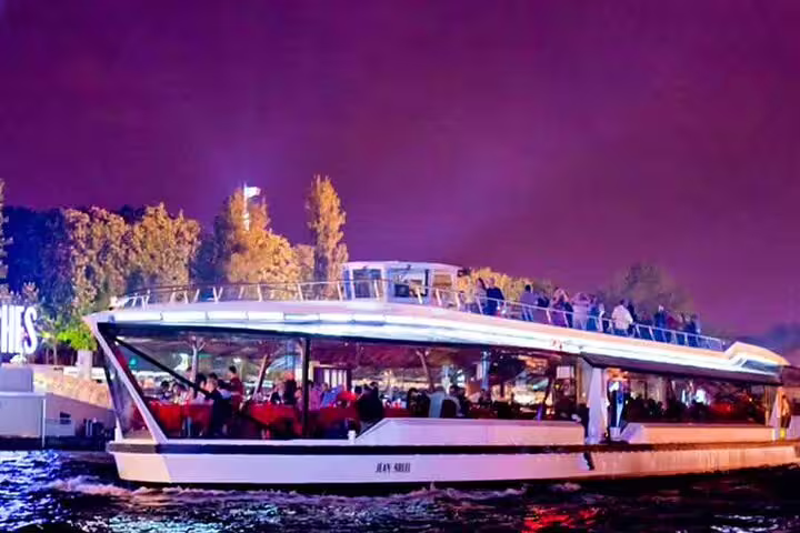 Illuminated Seine River dinner cruise boat with guests dining inside and on deck at night in Paris