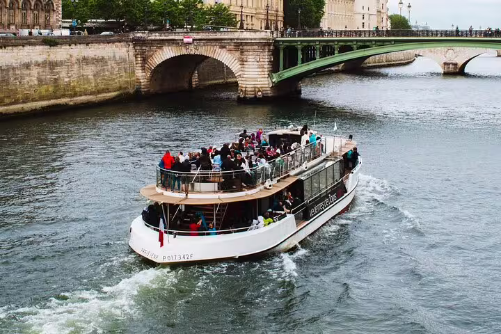 Tourist cruise boat filled with passengers sailing on the Seine River in Paris with historic bridge in background