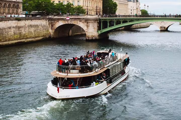 Tourist cruise boat packed with visitors sailing on the Seine River in Paris with historic stone bridges