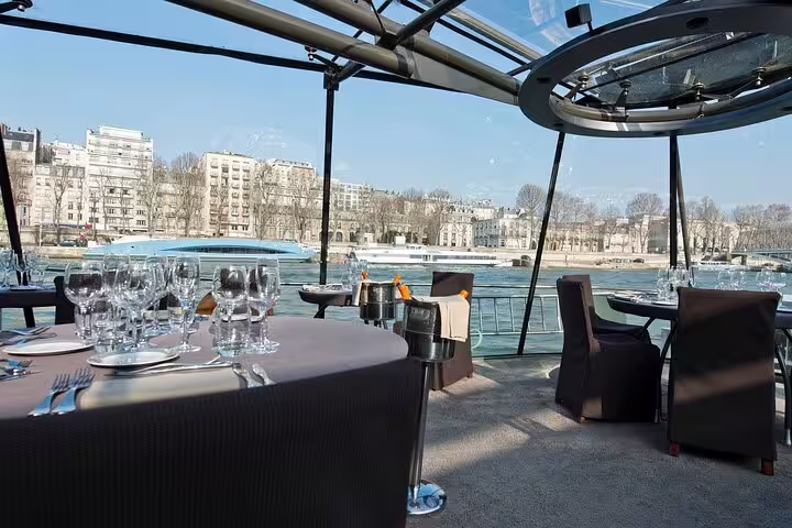 Elegant dining tables set with wine glasses on a Seine River cruise boat with Paris cityscape views