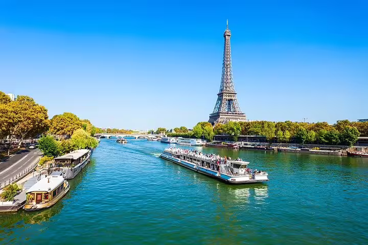 Tourist cruise boat on the Seine River with the Eiffel Tower rising above lush green trees in Paris