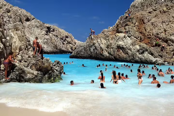 Tourists swim and relax in the turquoise waters surrounded by rocky cliffs at Seitan Limania beach in Crete.