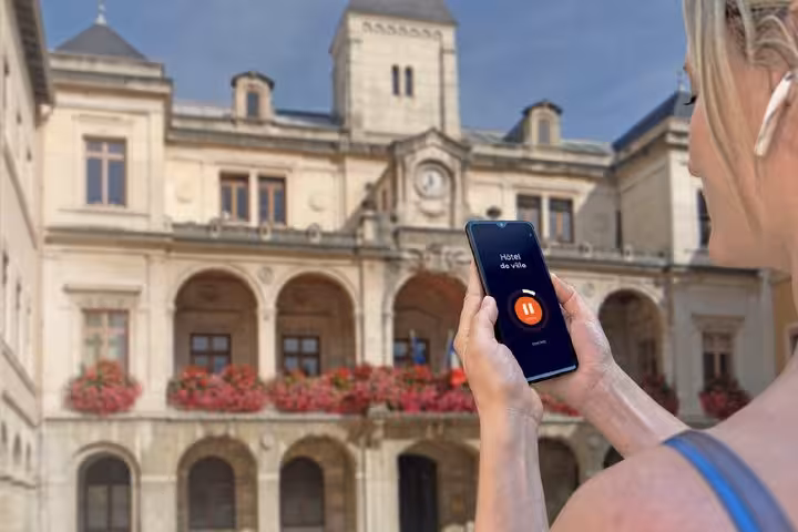 Tourist holding smartphone with audio guide app in front of Hôtel de Ville in Vienne, France