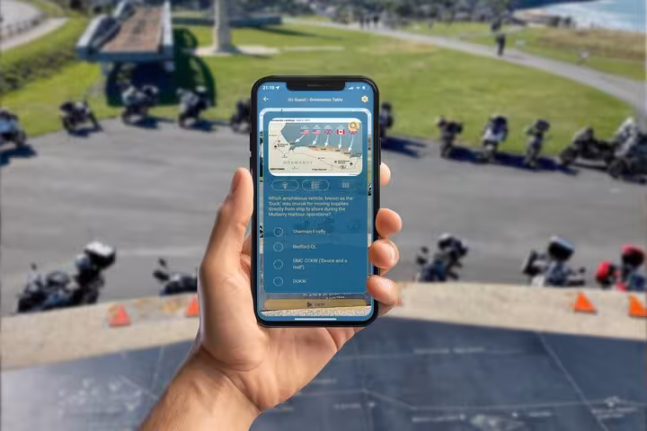 Hand holding smartphone displaying D-Day Arromanches mobile game quiz with motorcycles and memorial in background