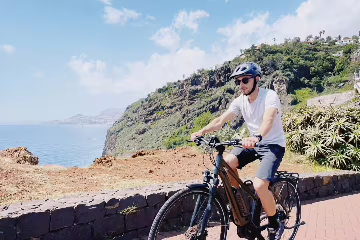 Cyclist enjoying a scenic self-guided e-bike tour from Funchal to Garajau with stunning ocean and coastal views.