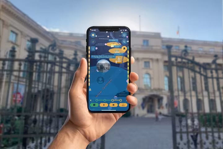 Hand holding smartphone with guided tour mobile app in front of historic Bucharest palace building