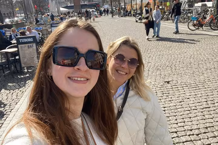 Two women taking a selfie on a sunny cobblestone square in Copenhagen with a Tuborg bar in the background