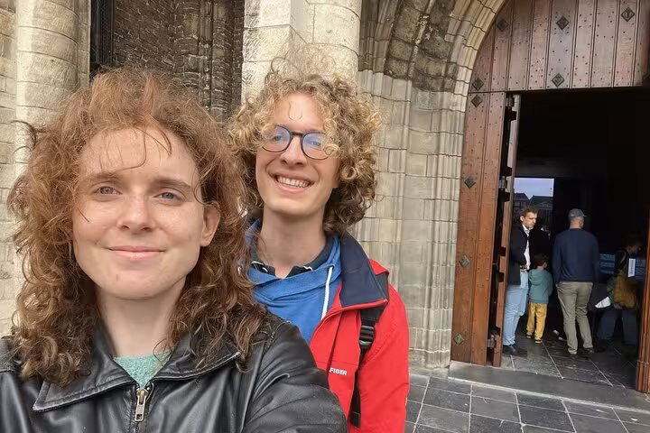 Two curly-haired visitors smiling outside a historic Gothic church entrance in Delft