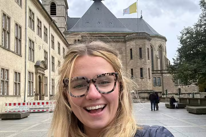 Smiling woman with glasses on a self-guided walking tour in Luxembourg City plaza with historic church