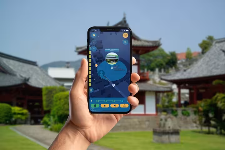 Hand holding smartphone with self-guided walking tour app in front of traditional Nagasaki temple buildings