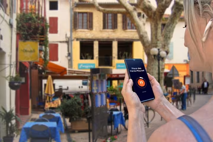 Tourist holding smartphone with audio guide app at Place des Frères Mounet in Orange, France