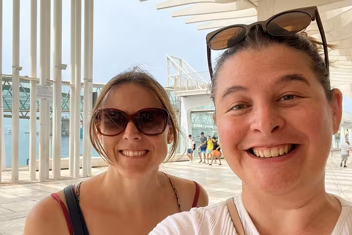 Two smiling women taking a selfie during a self-guided walking tour near a modern waterfront building