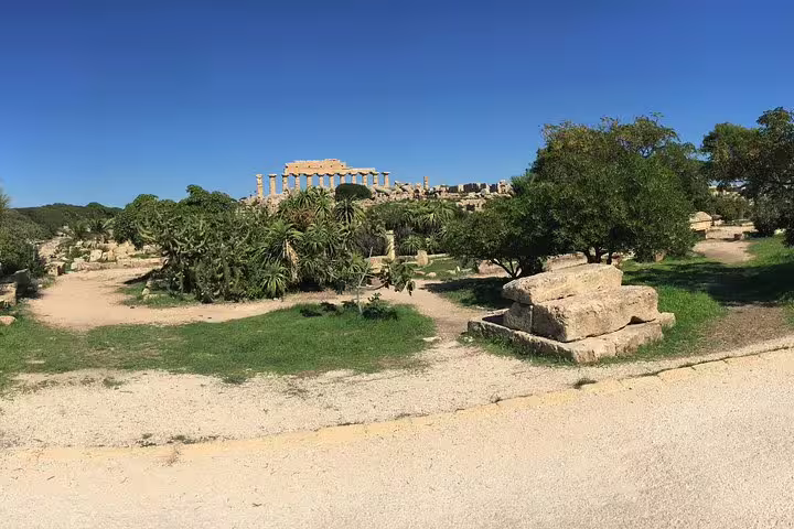 Ancient Greek temple ruins at Selinunte Archaeological Park with scattered stones and Mediterranean greenery under a clear blue sky