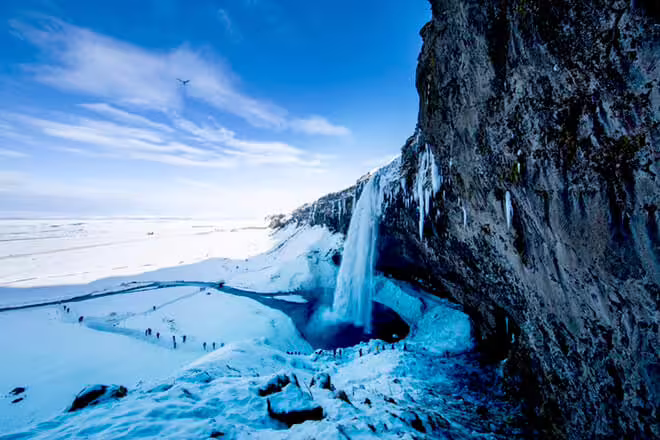 Seljalandsfoss waterfall frozen in winter with visitors exploring snow-covered Iceland south coast