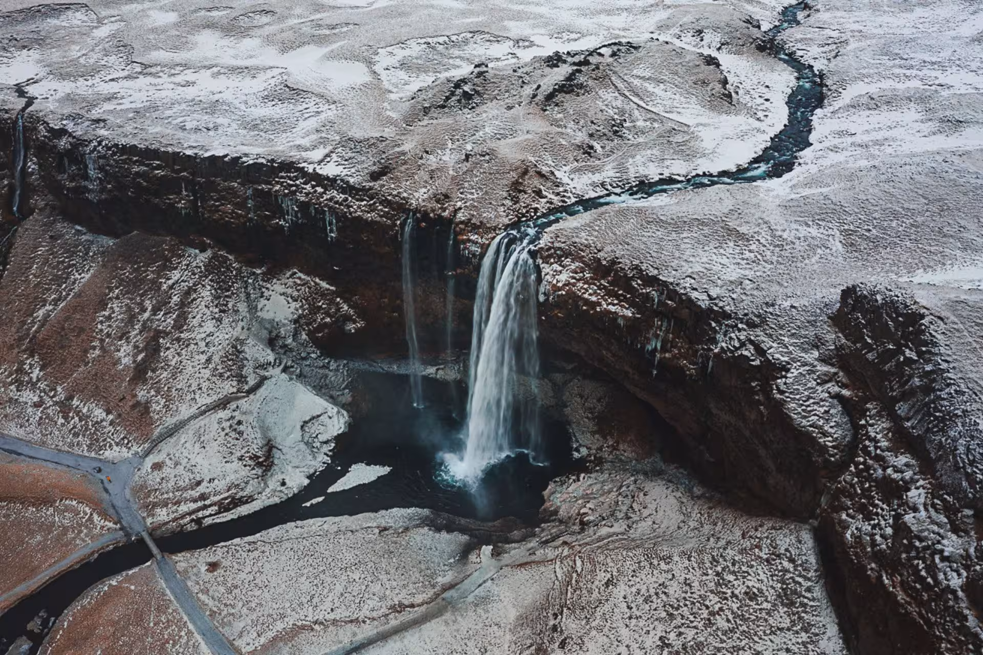 Aerial winter view of Seljalandsfoss waterfall cascading into a dark pool on Iceland's snow-dusted south coast