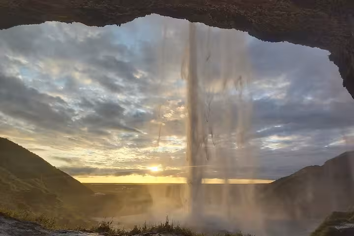 View from behind Seljalandsfoss waterfall with golden sunset over Iceland's south coast landscape