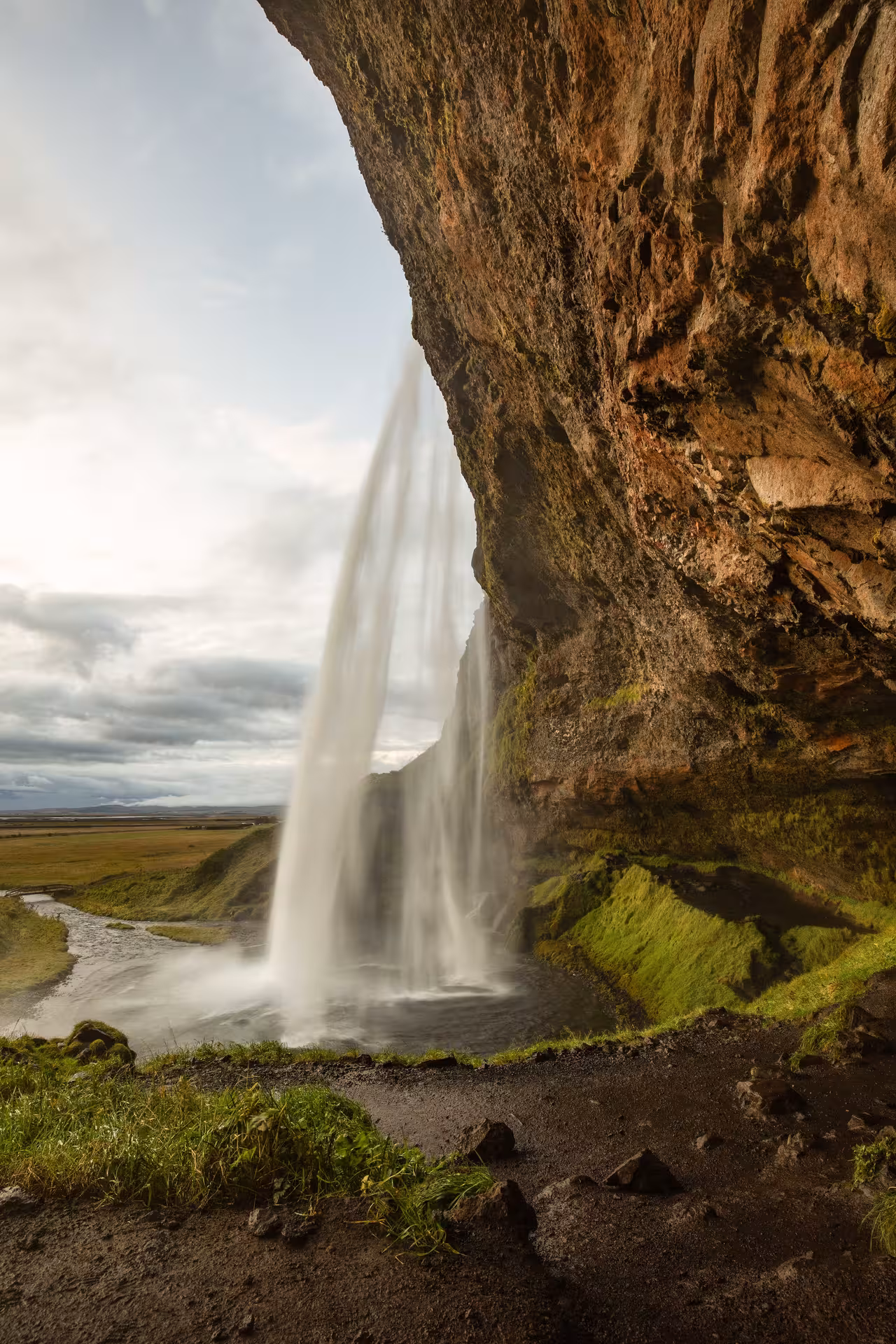 View from behind Seljalandsfoss waterfall cave on Iceland's South Coast, showing cascading water and green moss