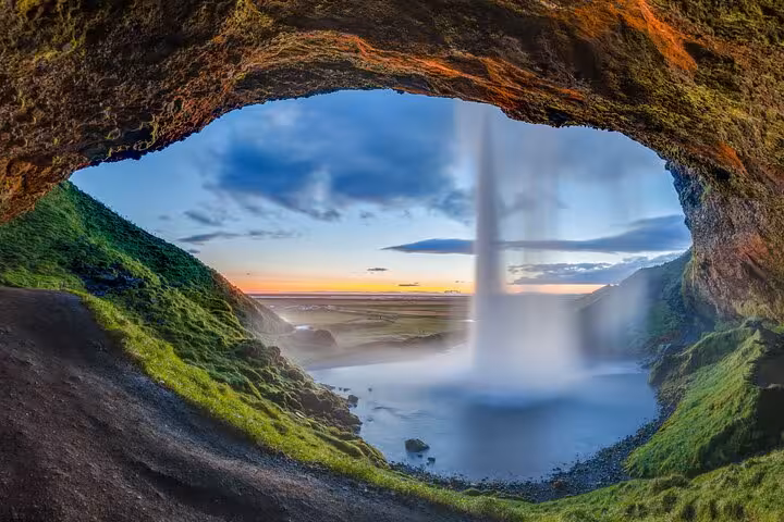 View from behind Seljalandsfoss waterfall on Iceland's South Coast at sunset with green cliffs and plains