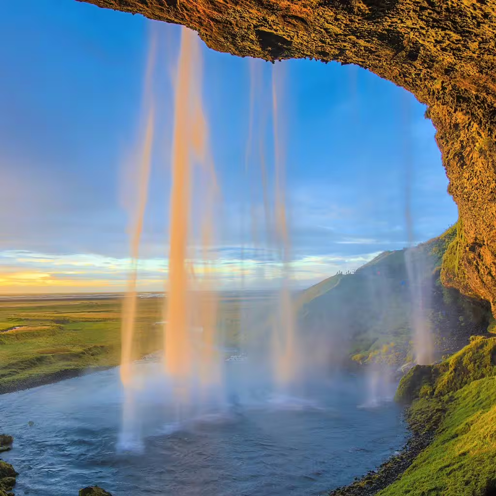 View from behind Seljalandsfoss waterfall on Iceland's South Coast at golden hour sunset