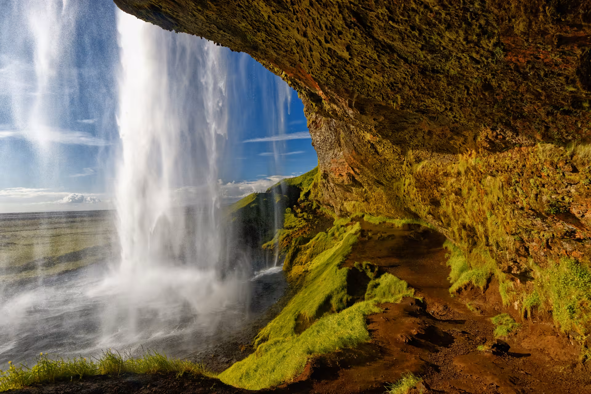 View from behind Seljalandsfoss waterfall cave on Iceland's South Coast, with mossy cliffs and blue sky
