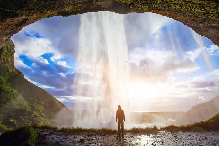 Silhouette of person standing behind Seljalandsfoss waterfall cave on Iceland South Coast tour
