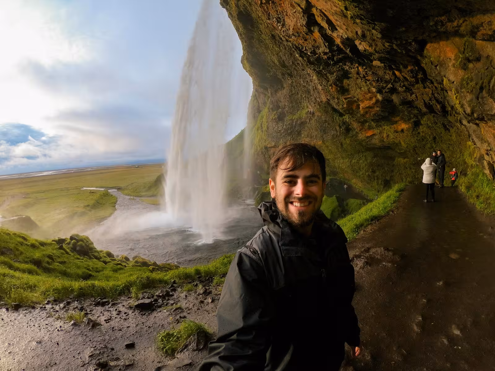Tourist smiling near Seljalandsfoss waterfall, enjoying a unique perspective from behind the cascading waters in Iceland.