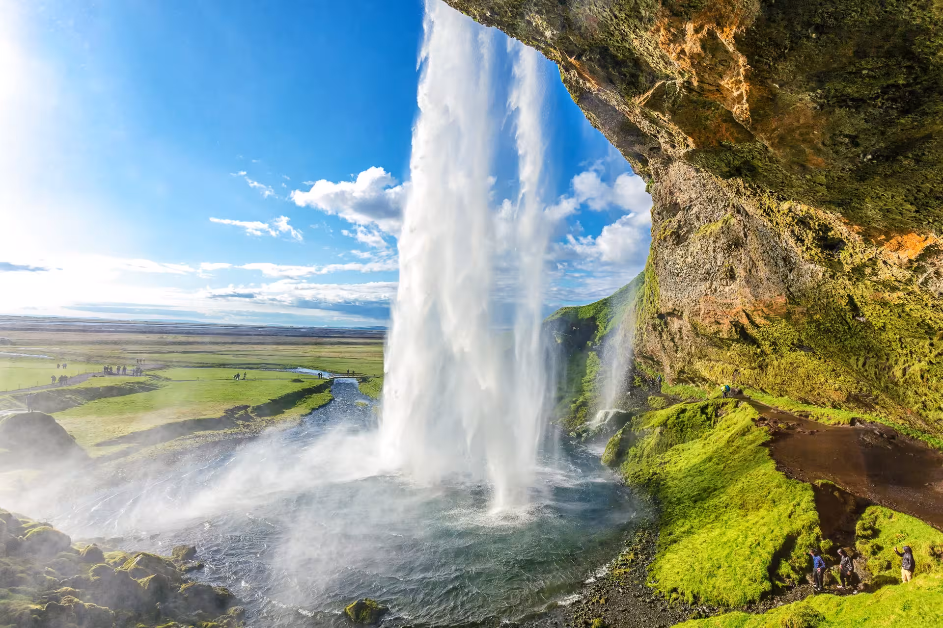 Seljalandsfoss waterfall in South Iceland with tourists exploring behind the cascading water under a bright blue sky.
