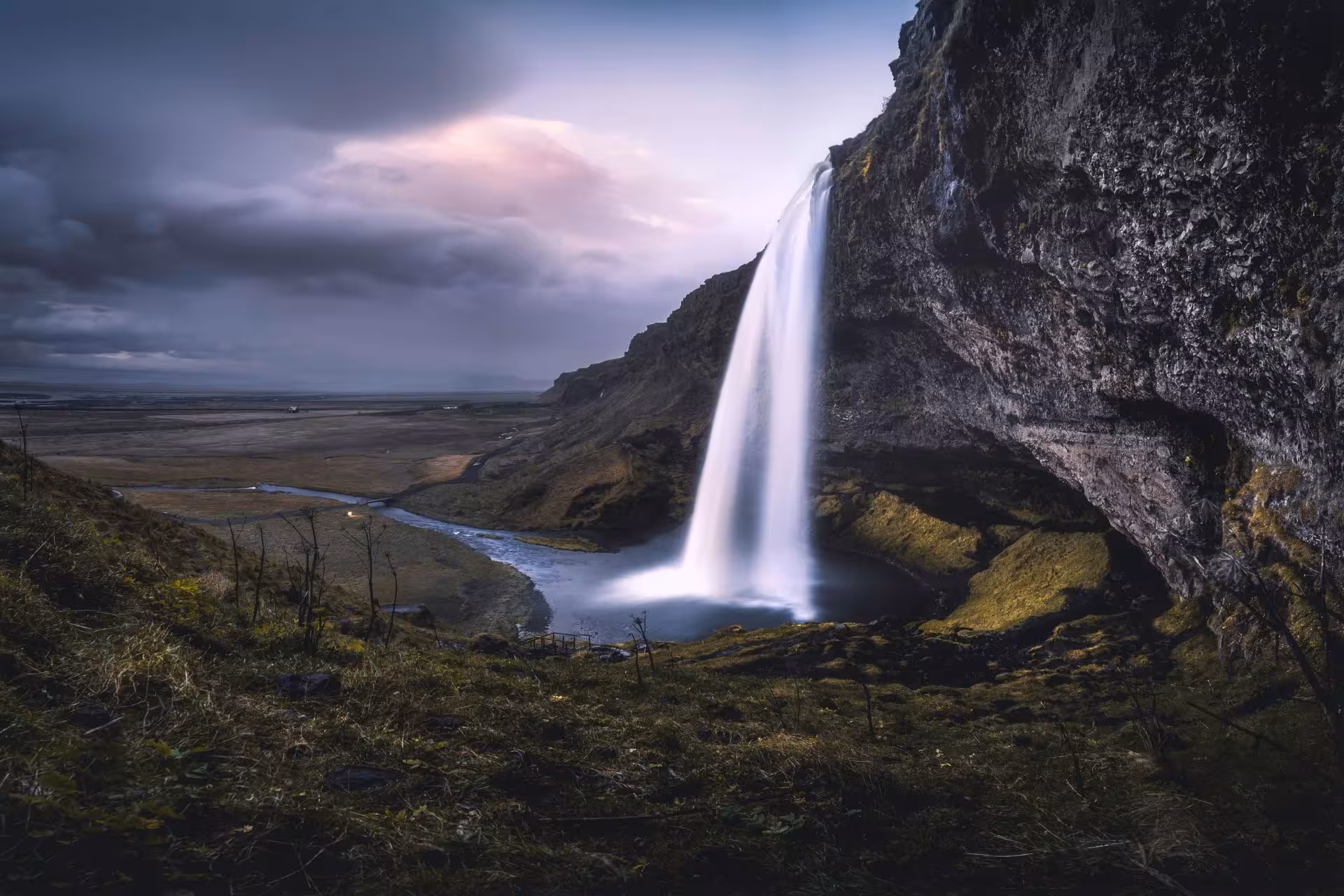 Seljalandsfoss waterfall cascading down cliffs into a river on Iceland's south coast at dusk