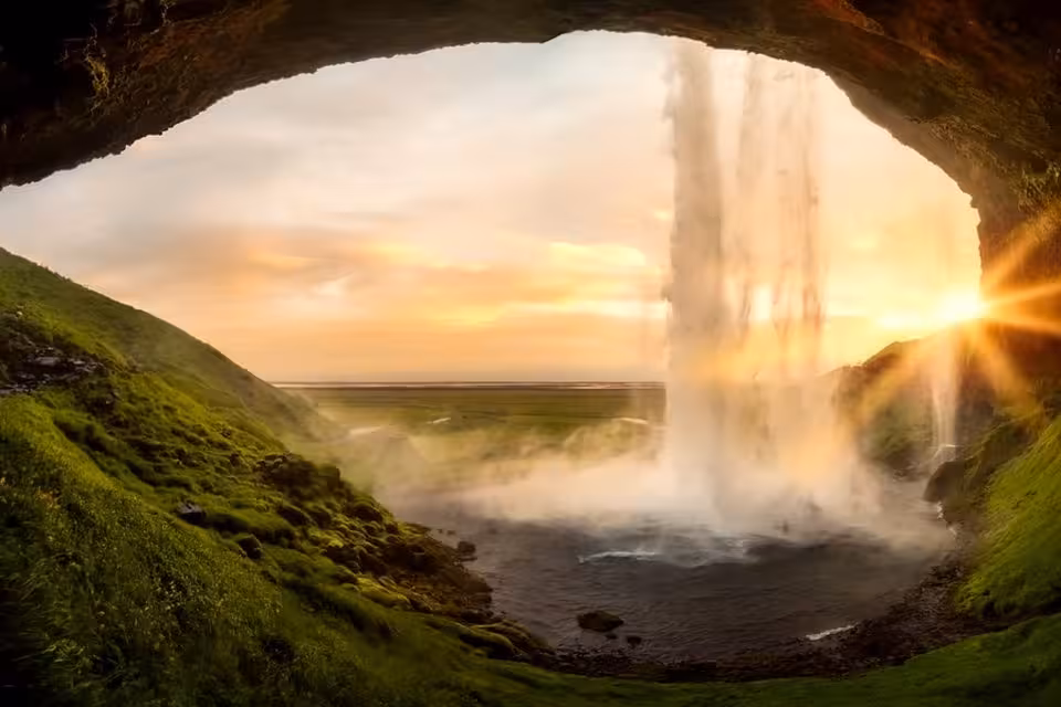 View from behind Seljalandsfoss waterfall at golden sunset on Iceland's South Coast