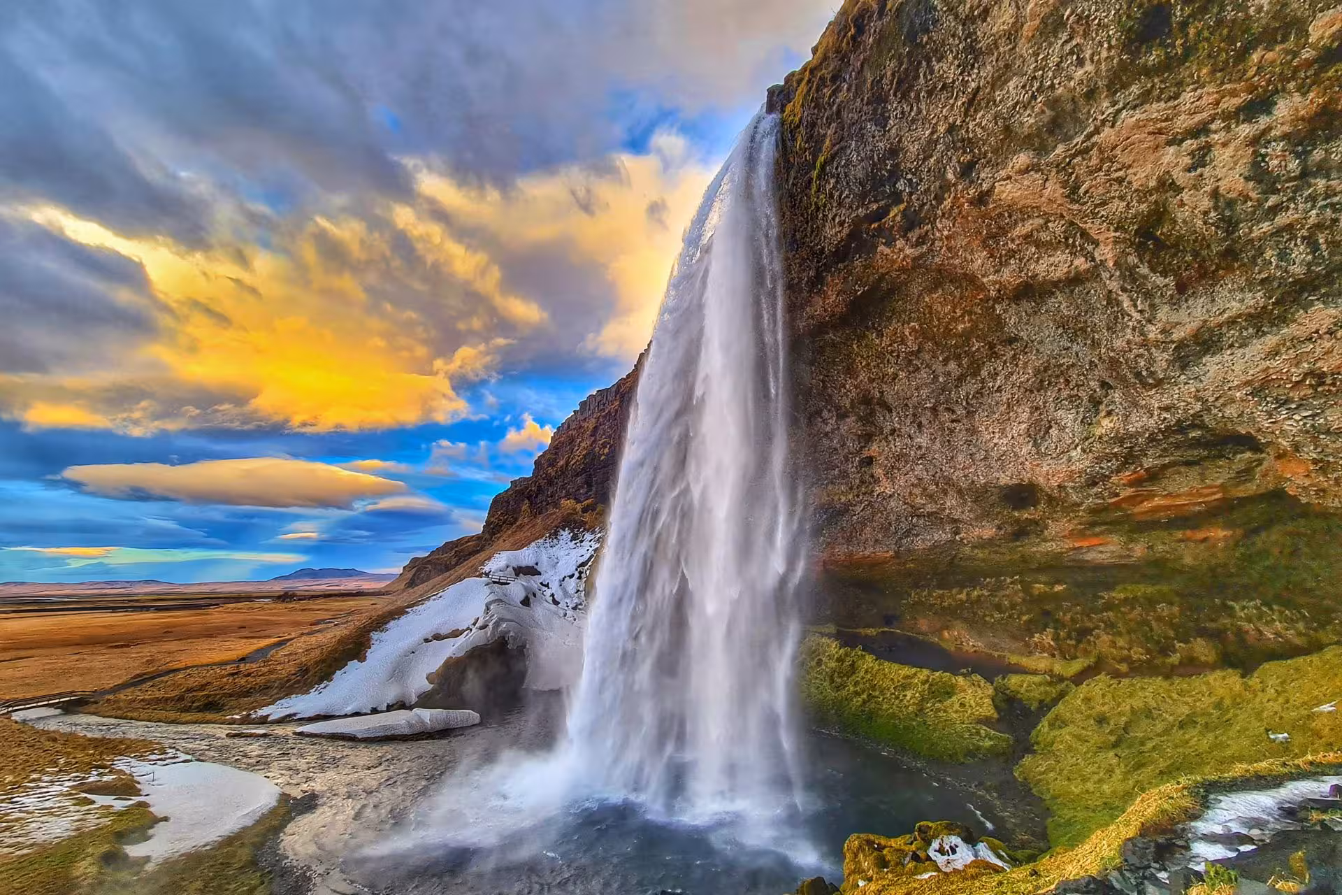 Seljalandsfoss waterfall cascading over mossy cliffs at sunset with snowy ground on Iceland's south coast