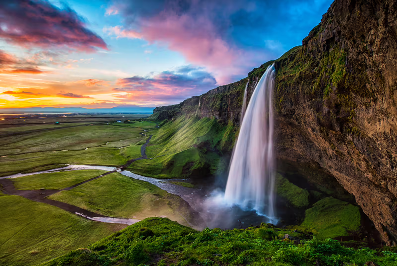 Seljalandsfoss waterfall cascading over green cliffs at sunset on Iceland's South Coast