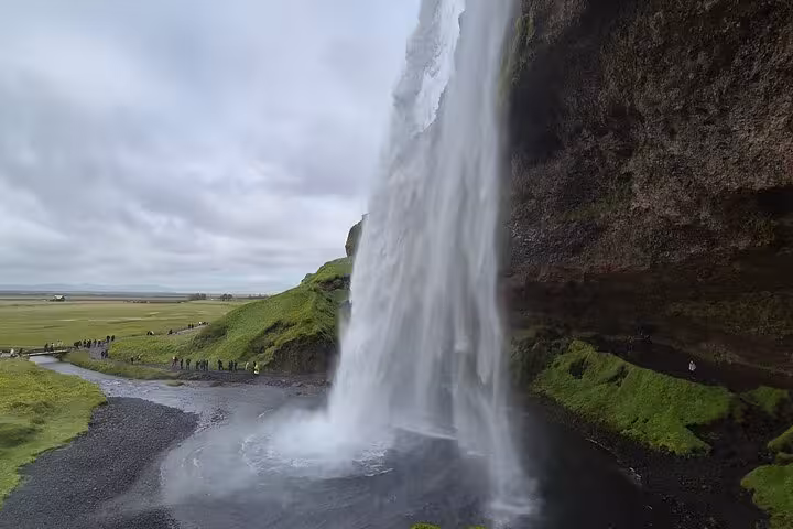 Seljalandsfoss waterfall viewed from behind on Iceland's South Coast with visitors on path below